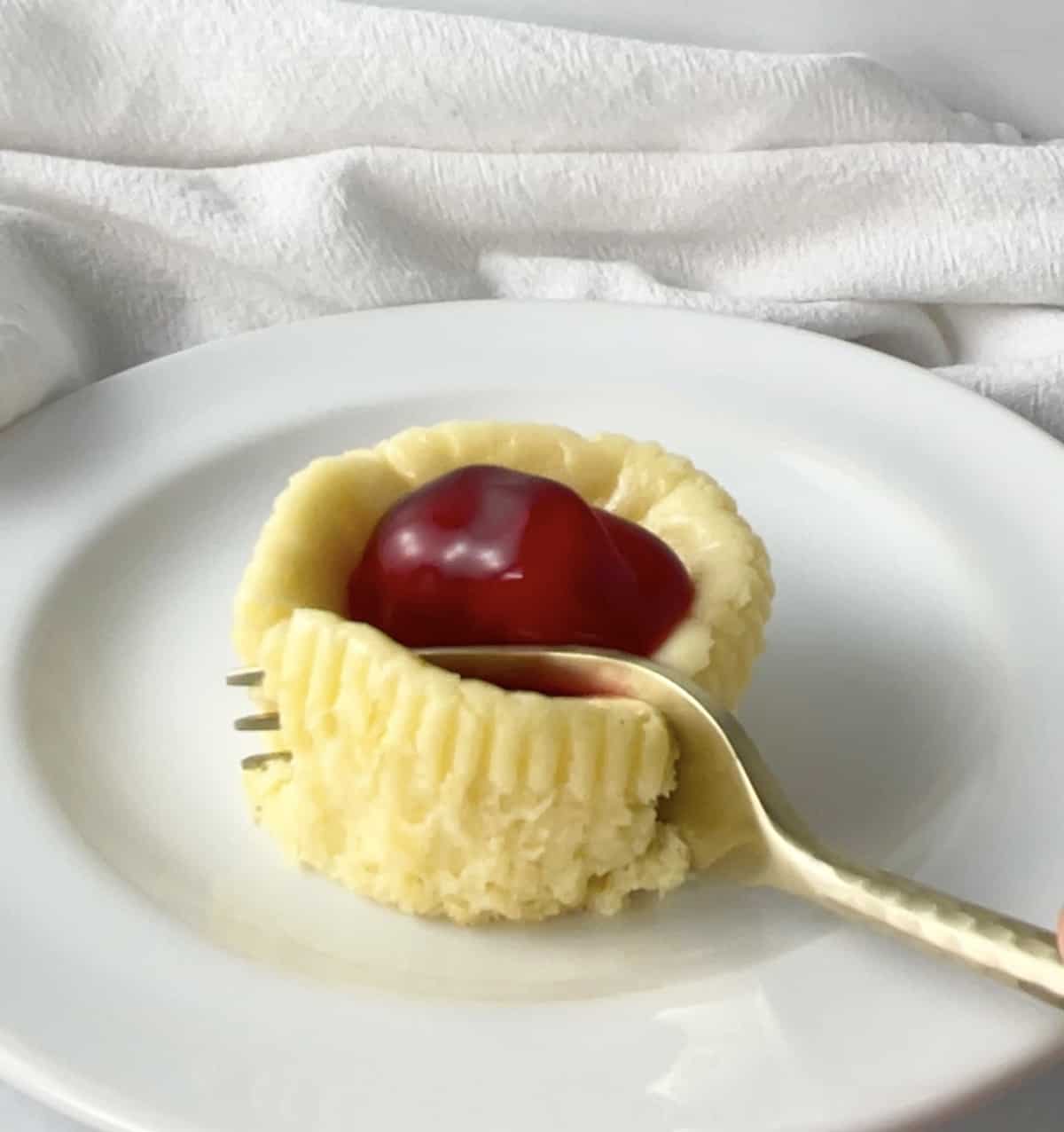 Mini cheesecake on a small white plate with gold fork.