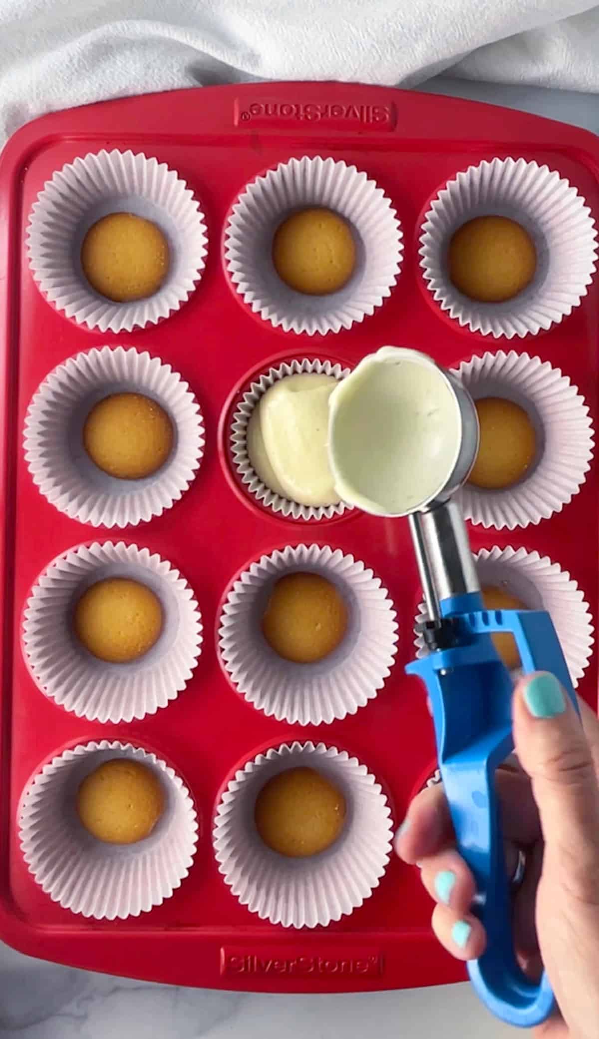 Scooping cheesecake batter into muffin pan with cupcake liners and vanilla wafer crust.