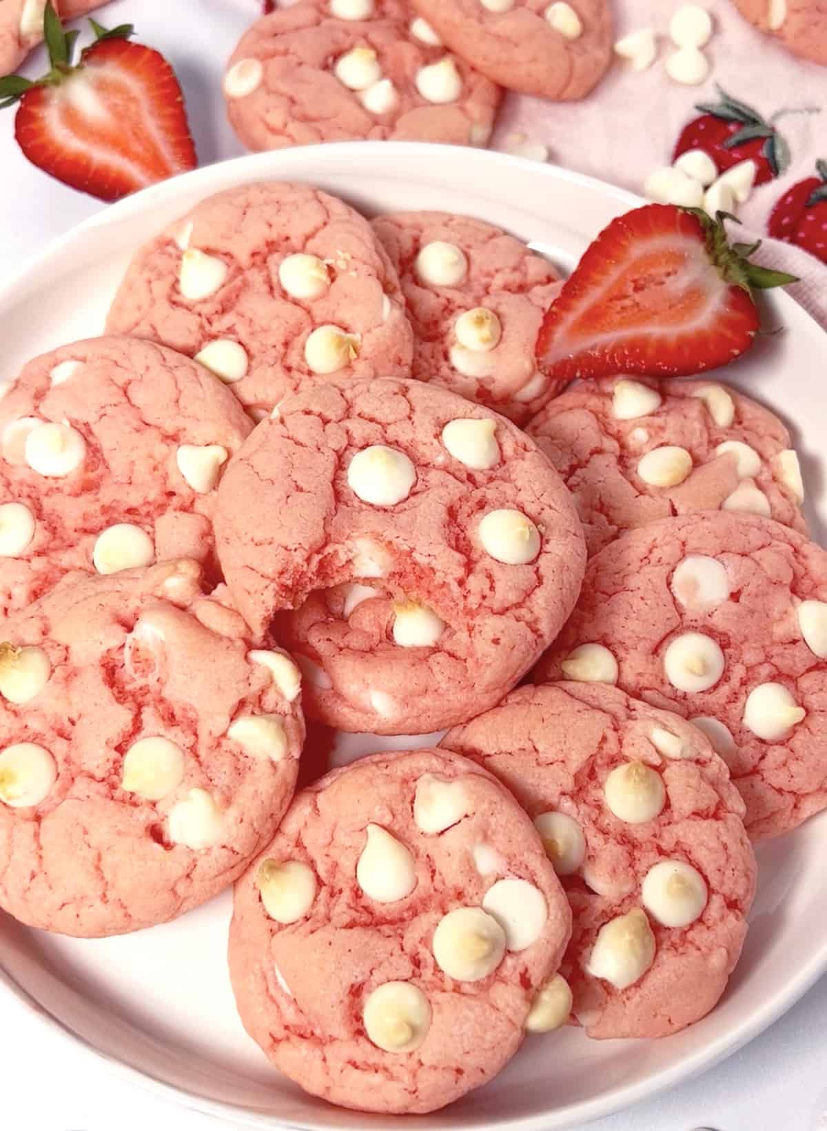 Big pile of pretty pink cake mix cookies on a plate with strawberries on the side.