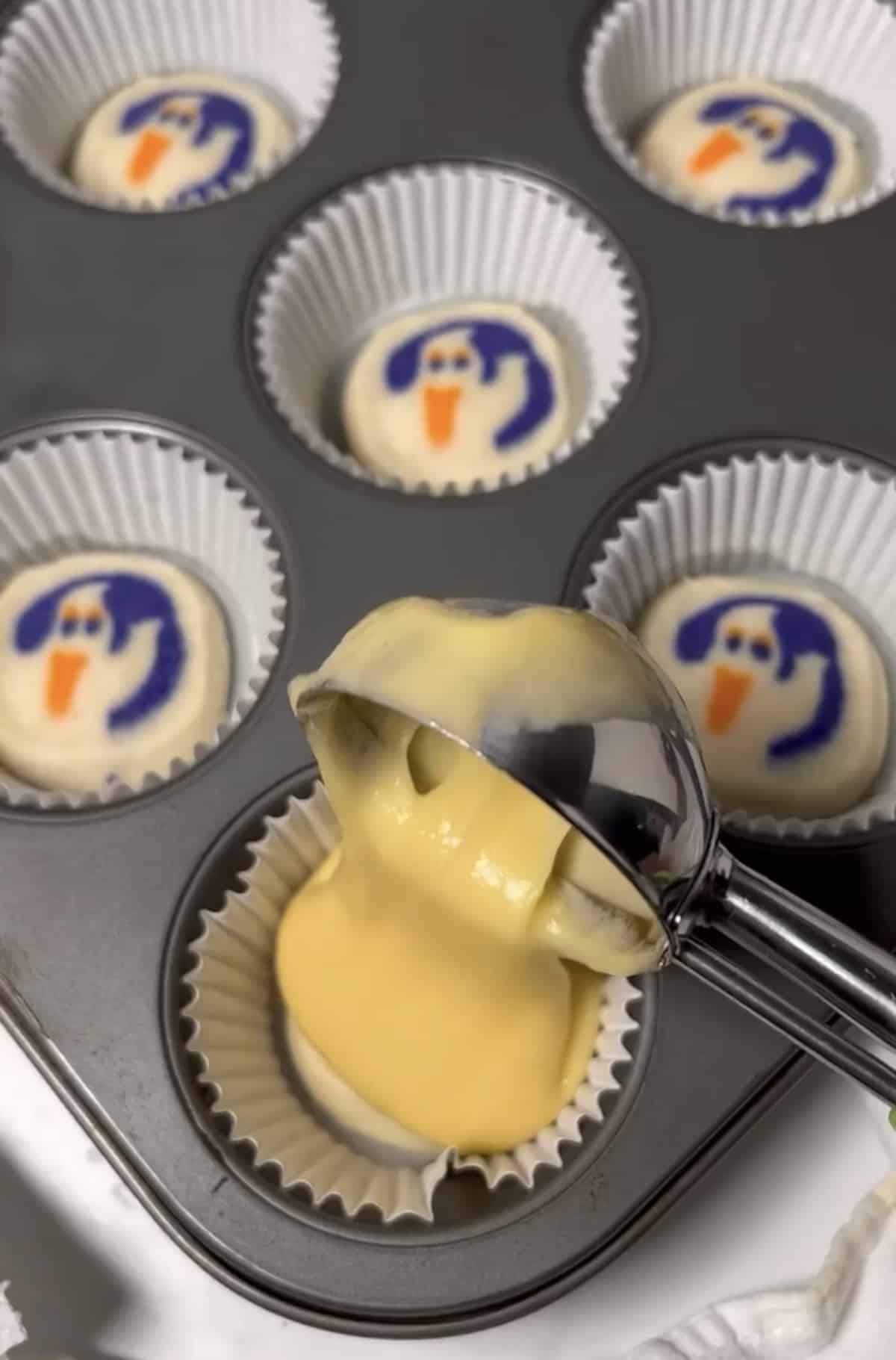 Scooping cake batter into cupcake pan with liners and Halloween cookie.