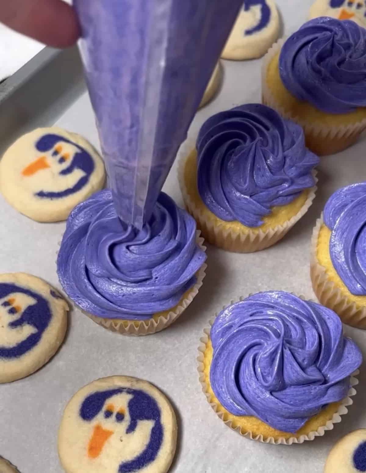 Piping purple buttercream frosting onto cupcake.