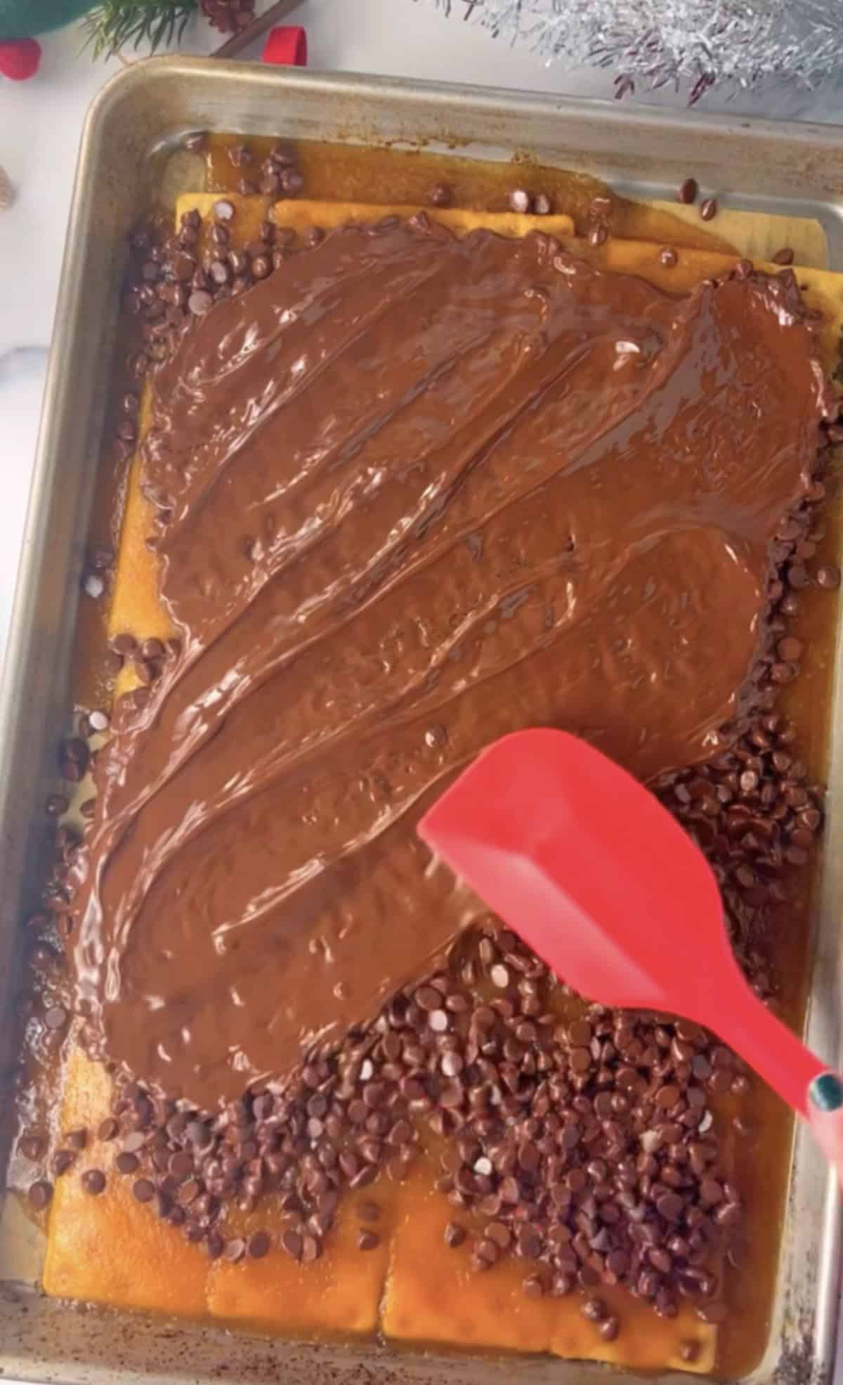 Spreading melted chocolate chips over cracker toffee with red spatula.