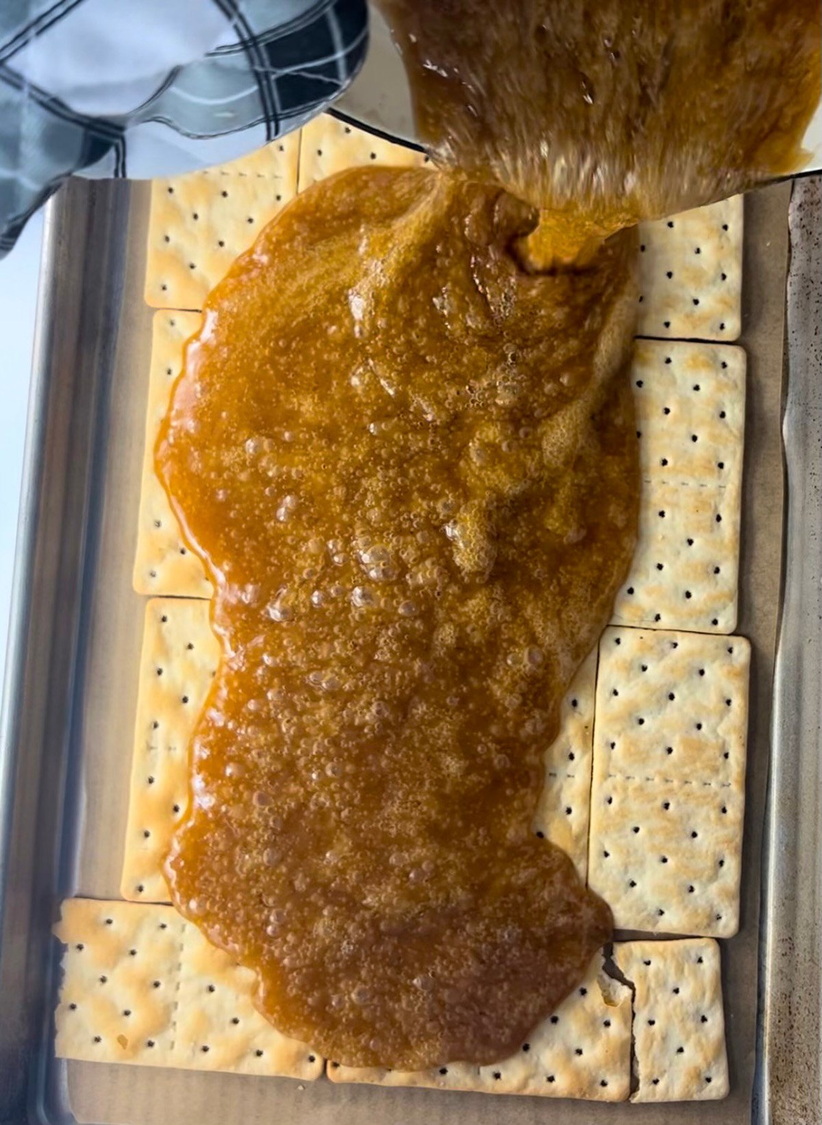 Hot toffee poured over crackers on a baking sheet pan.