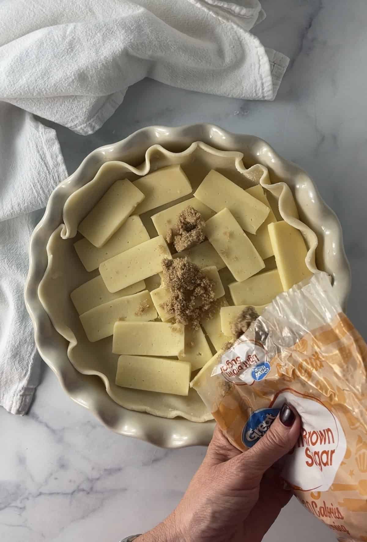 Pouring brown sugar over cheese slices in pie crust.