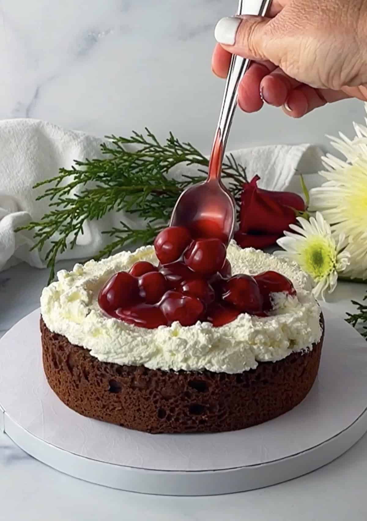 Spooning cherry pie filling onto whipped cream topped cake layer.