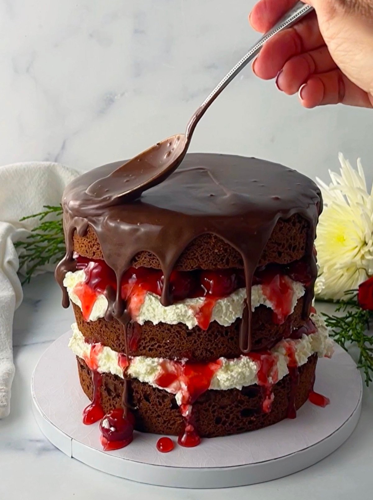 Pouring chocolate ganache over three layer black forest cake.