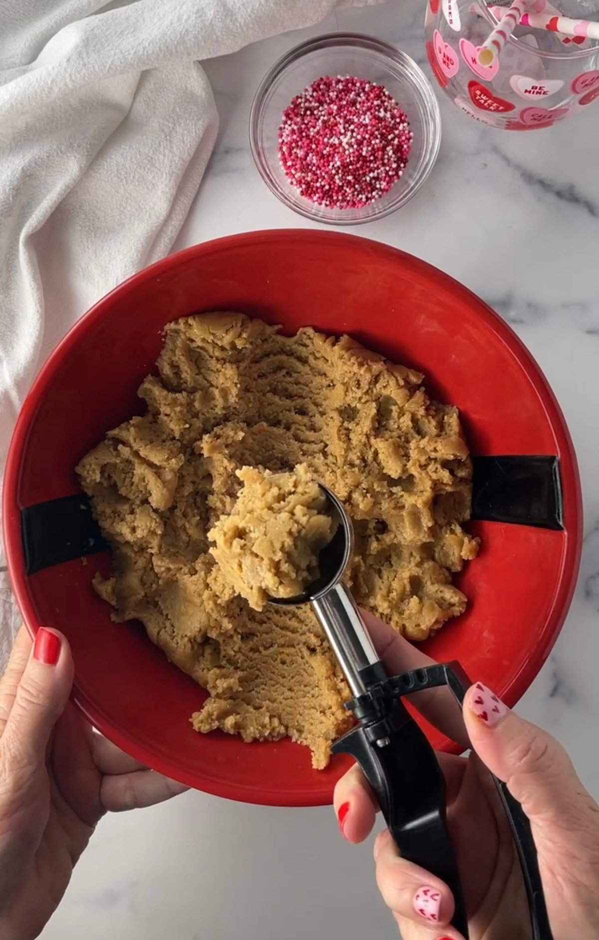 Peanut butter cookie dough in red bowl with cookie scoop.