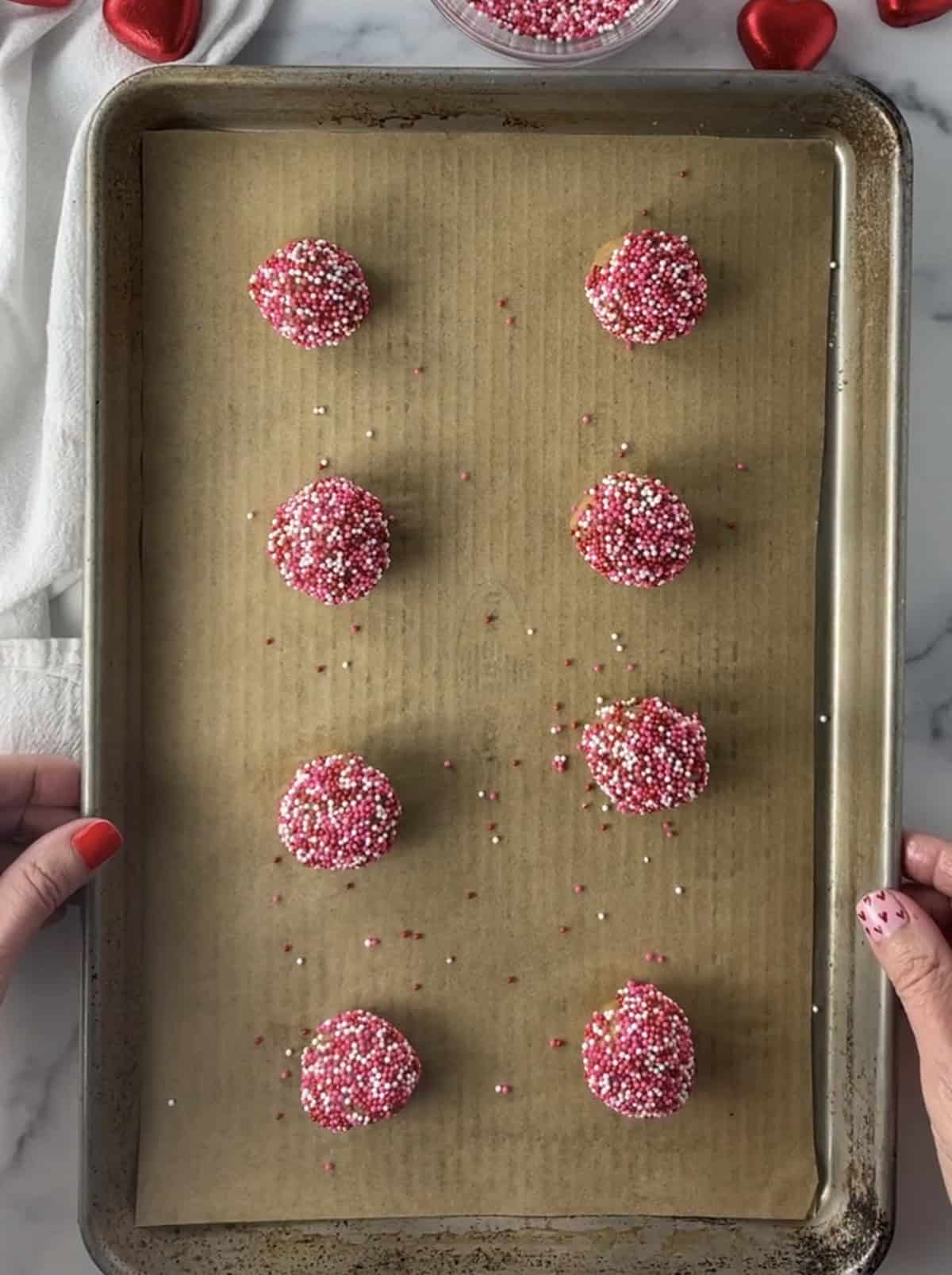 Cookie dough ball with sprinkles on cookie sheet.