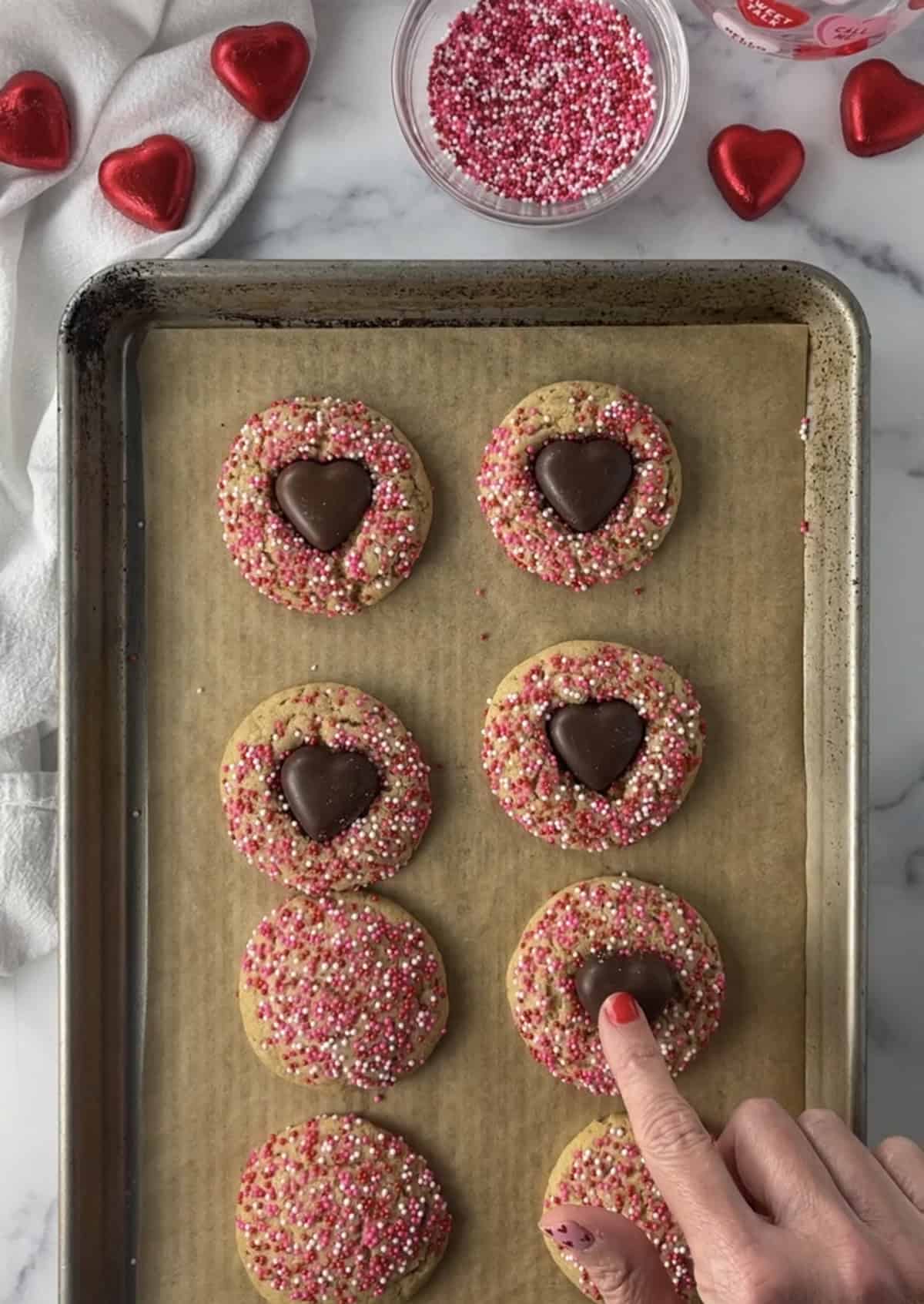 Placing heart chocolate on top of baked cookies.
