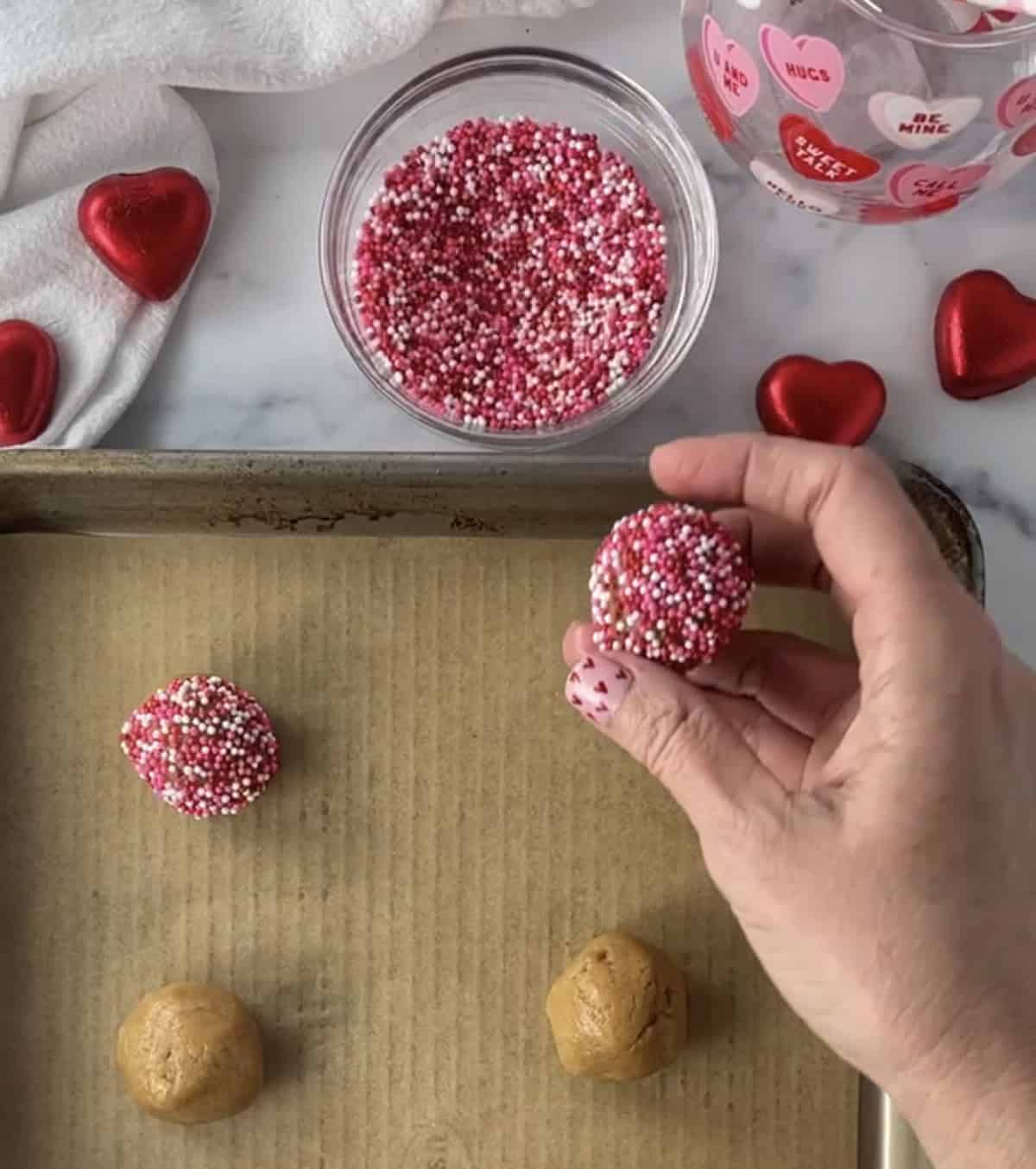 Rolling peanut butter cookie dough balls in sprinkles.