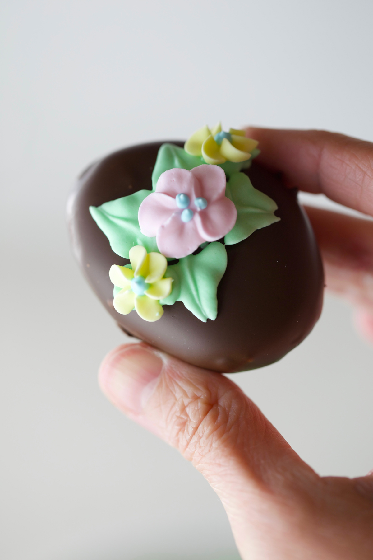 Hand holding one chocolate Easter egg with pretty royal icing flowers in pastel colors.