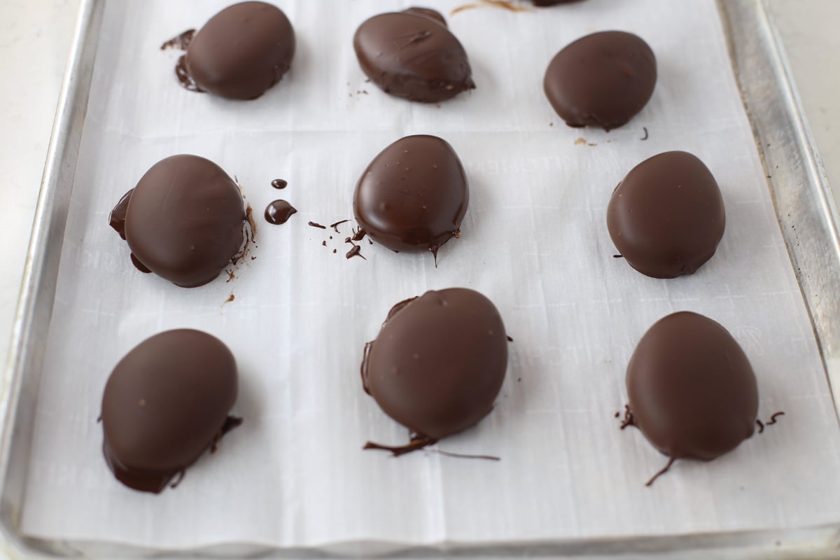 Peanut butter Easter eggs dipped in melted chocolate on a sheet pan with  parchment paper.
