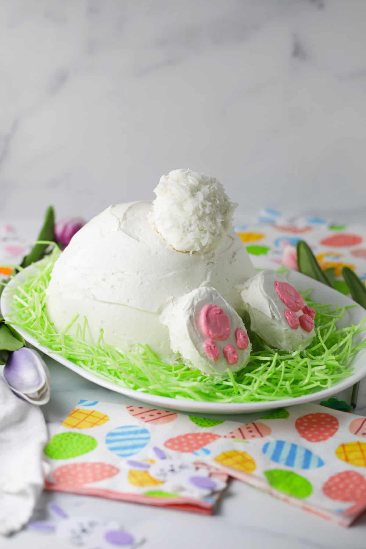 Easter bunny cake on a plate of green colored coconut flakes.