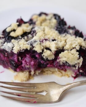 Blueberry pie bar on white plate with fork.