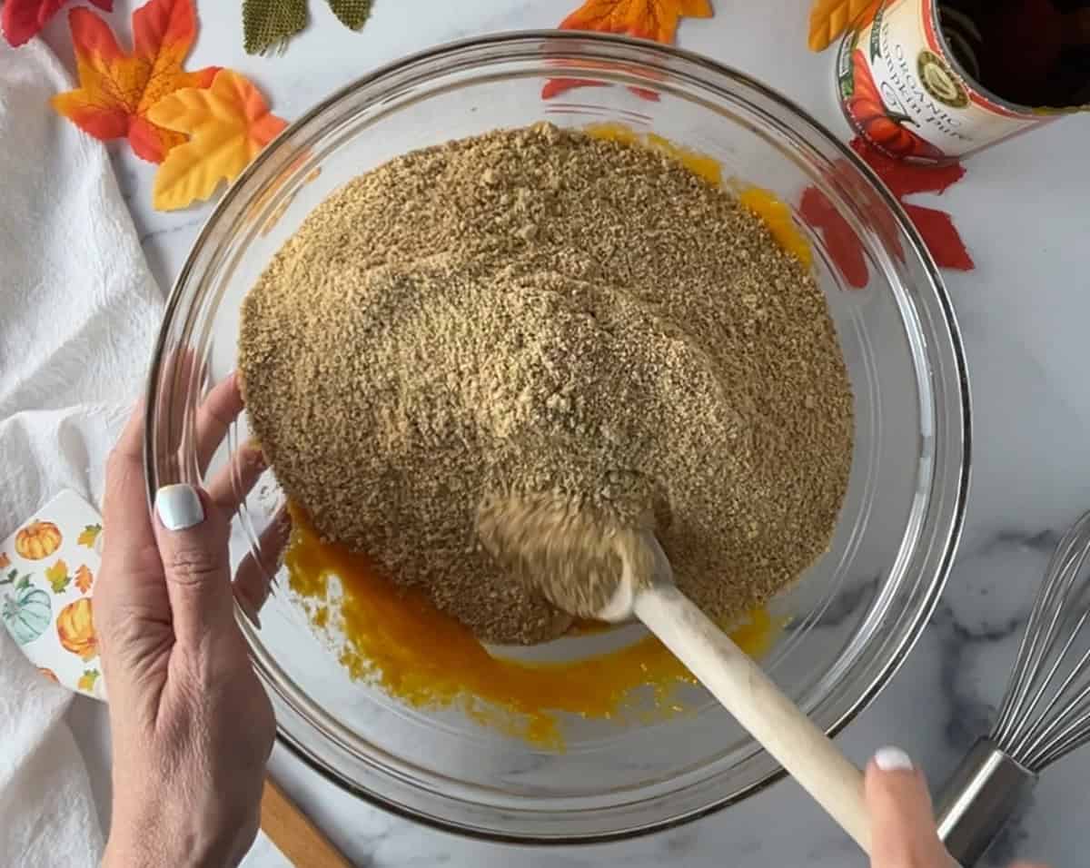 Graham cracker crumbs in a glass bowl with pumpkin and eggs.