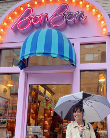 Adorable Swedish candy storefront in nyc with pink door, striped awning and neon lights with food blogger lise ode in front.