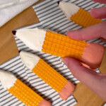 A hand holding another finished pencil cookie, ready to eat or share.