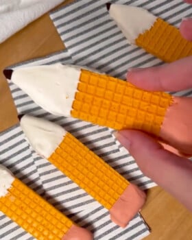 A hand holding another finished pencil cookie, ready to eat or share.