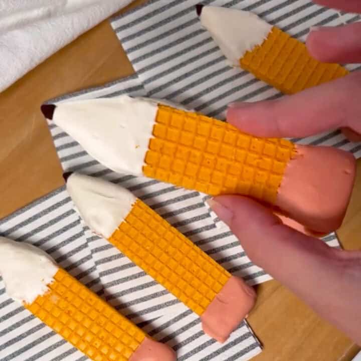 A hand holding another finished pencil cookie, ready to eat or share.