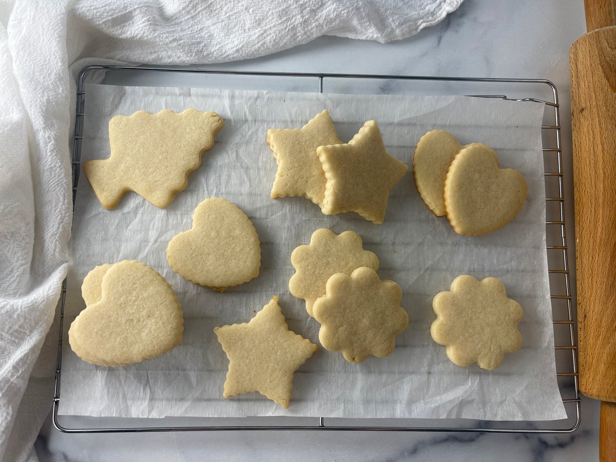 Assorted cut-out sugar cookies in various shapes cooling on the counter, unfrosted with golden edges.