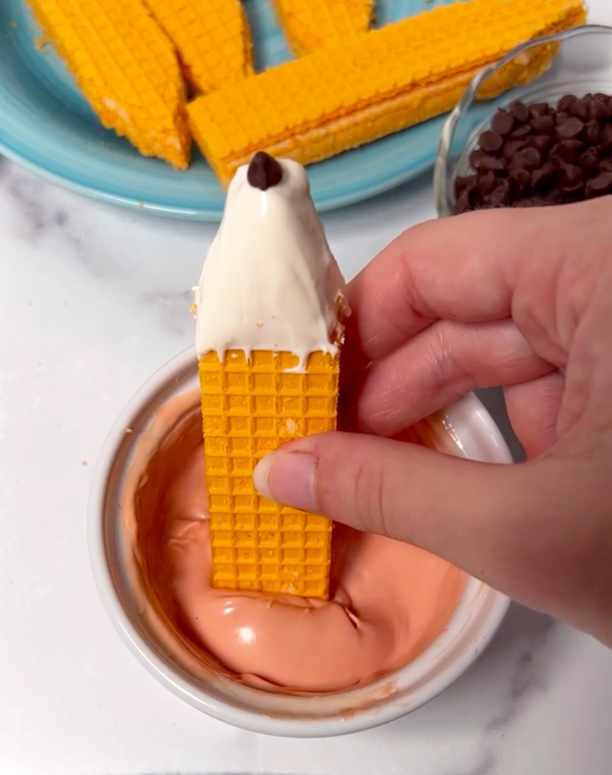 A sugar wafer being dipped into pink candy melts to form the eraser end of the pencil cookie.