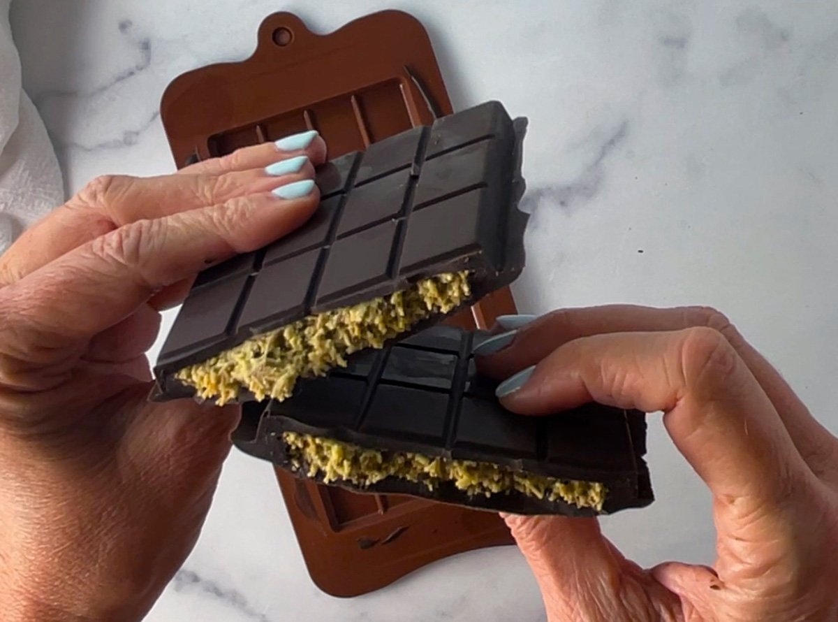 Hands holding a DIY Dubai pistachio chocolate bar broken in half to show the filling.