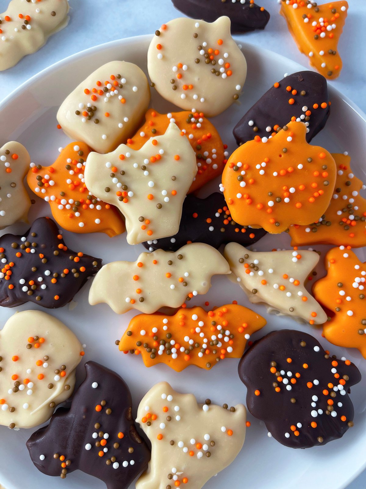 Halloween-themed frosted animal cookies topped with bright sprinkles, served on a plate.