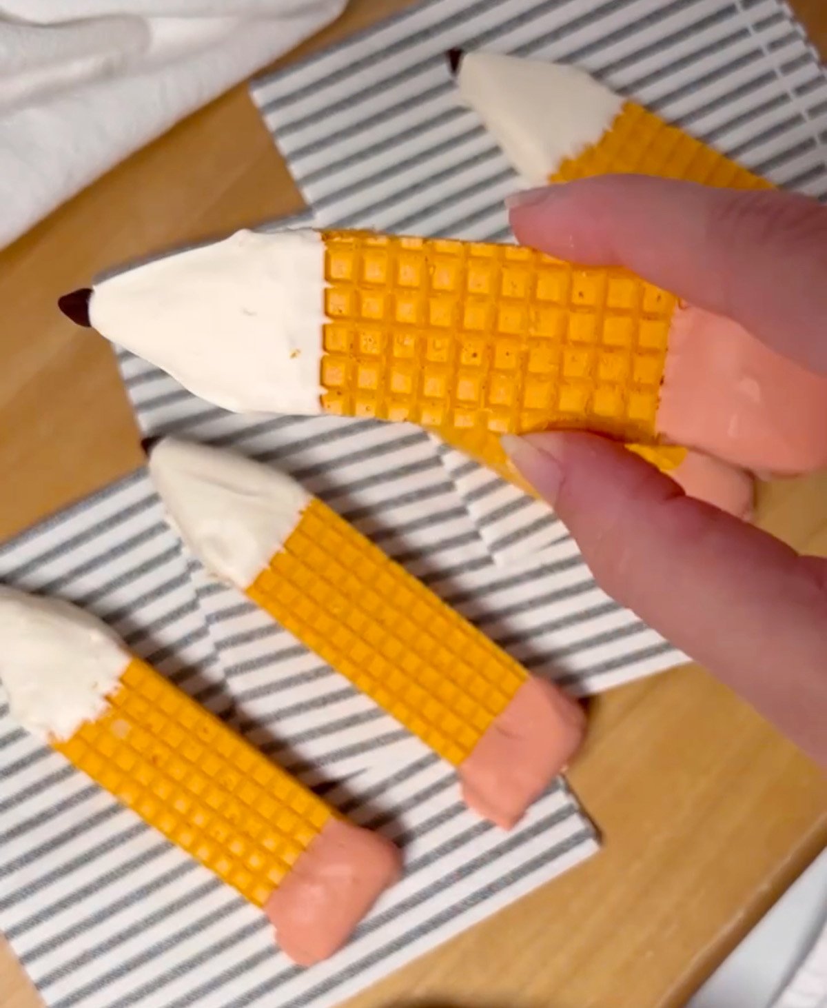A hand holding a finished pencil cookie decorated with candy melts and a chocolate chip tip.