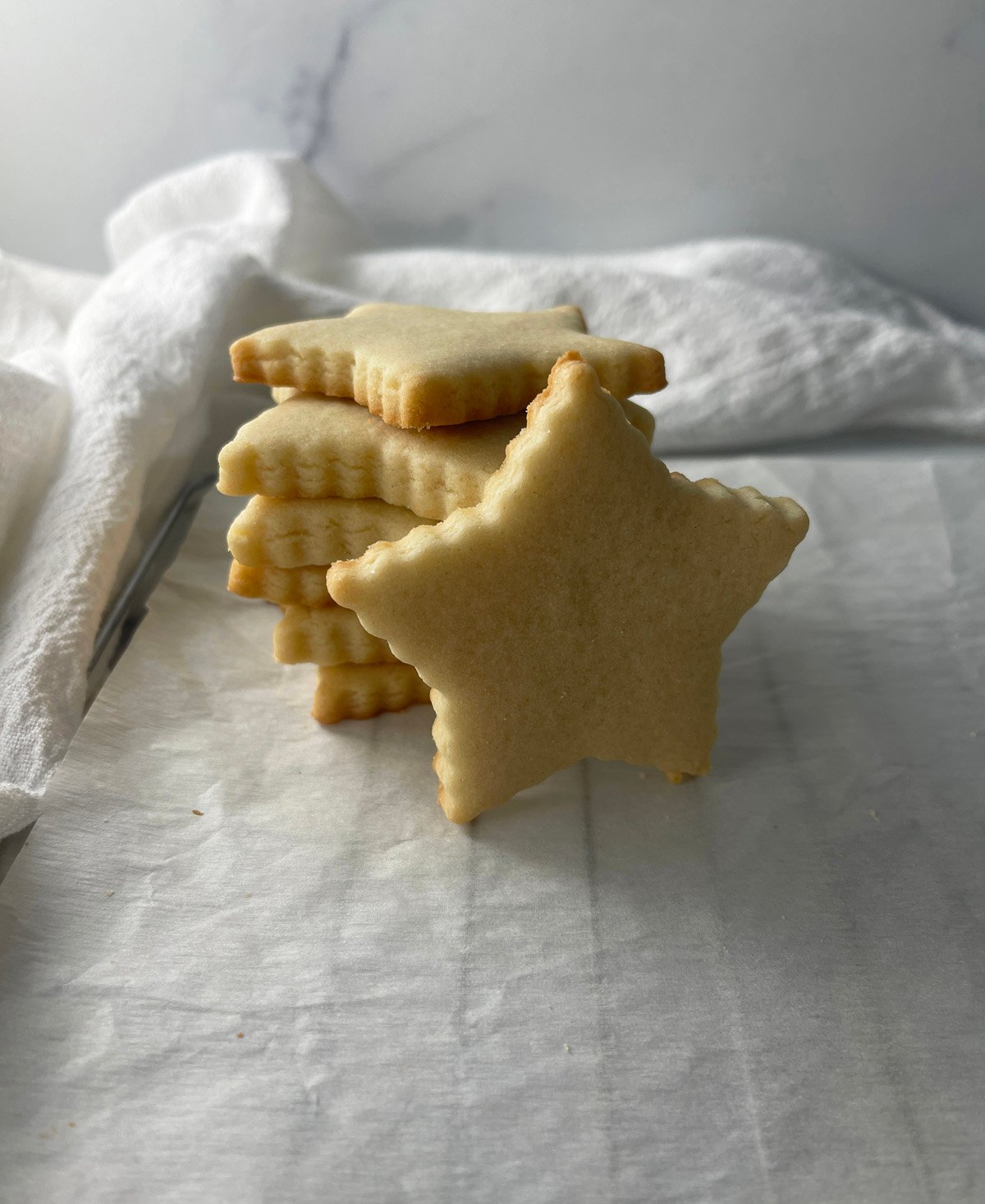 Stack of star-shaped sugar cookies with crisp edges resting on parchment paper.