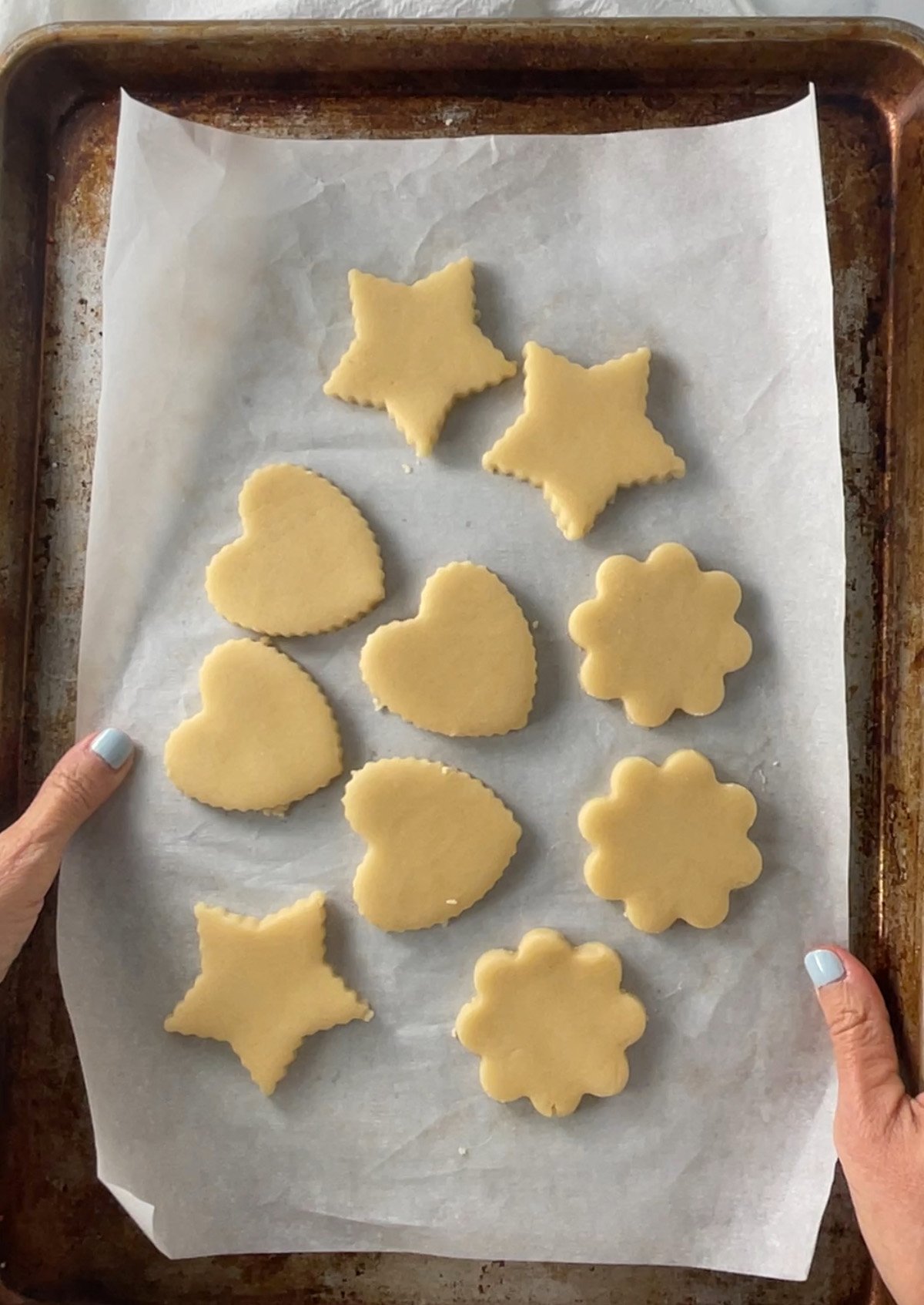 Unbaked cut-out sugar cookie shapes arranged on a baking sheet, ready to bake.