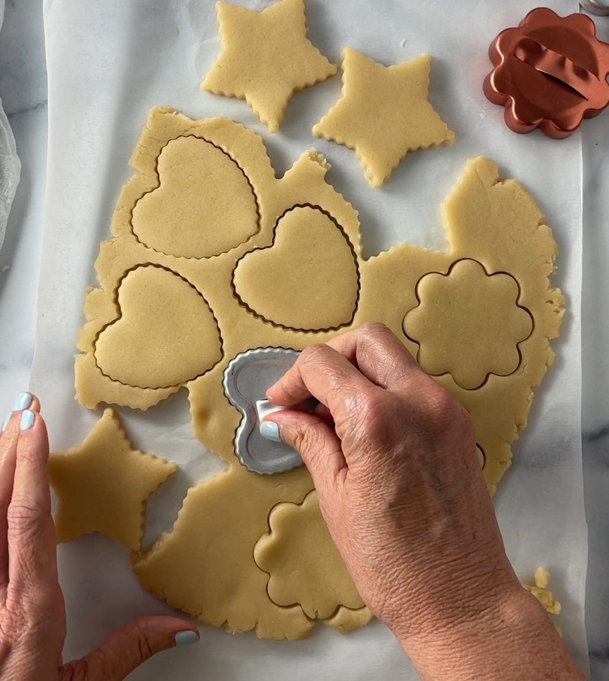 Rolled-out sugar cookie dough on parchment paper with cookie cutters cutting shapes.