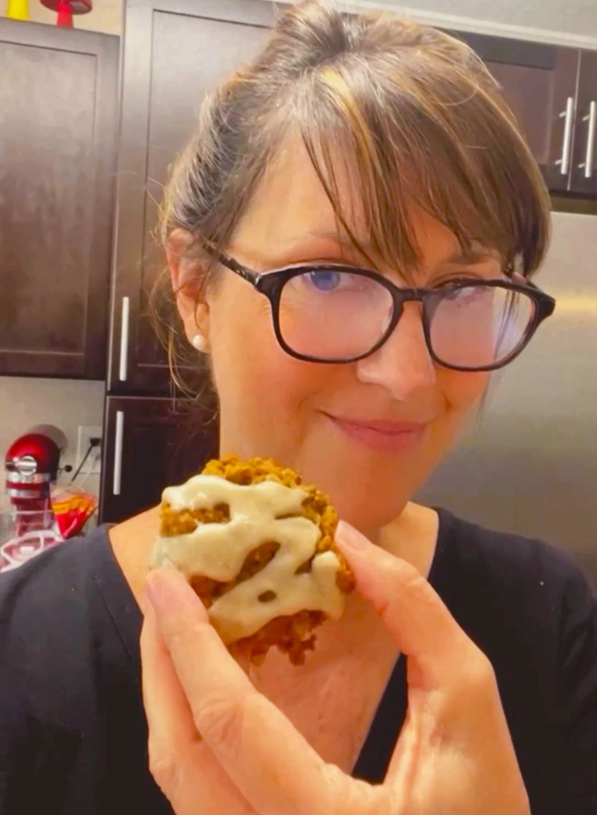 Close-up of Lise smiling while holding a cookie with a bite taken out to reveal chewy oatmeal pumpkin center.