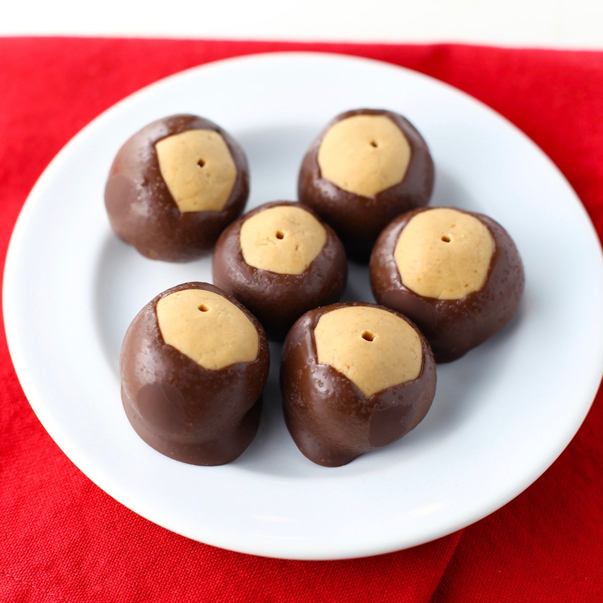 Stack of homemade buckeye candy balls showing smooth chocolate layer and peanut butter top.