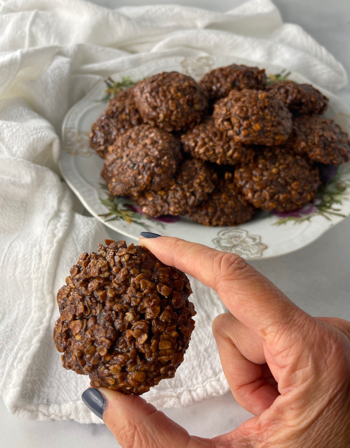 Hand holding a no bake chocolate oatmeal cookie with a plate of cookies in the background.