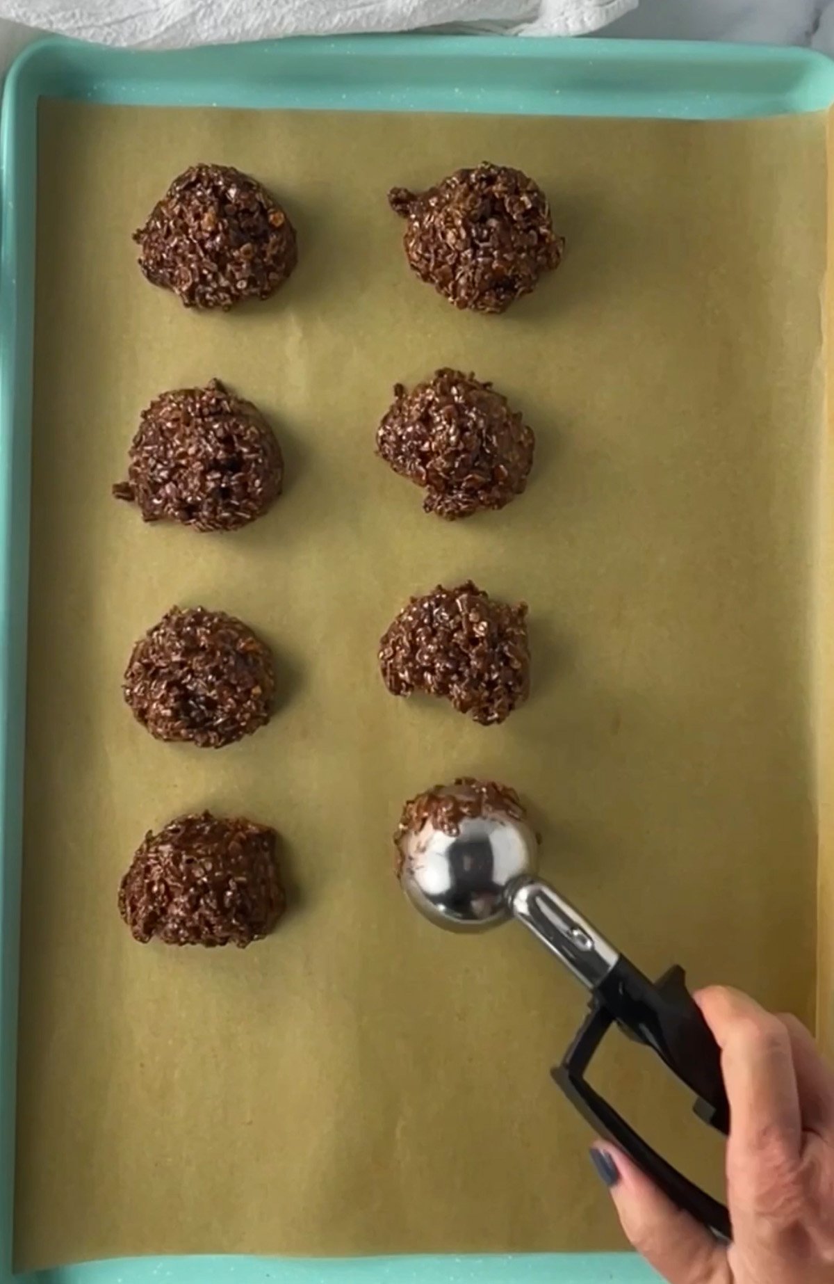 Scooping no bake chocolate oatmeal cookie mixture onto a baking sheet to cool and set.