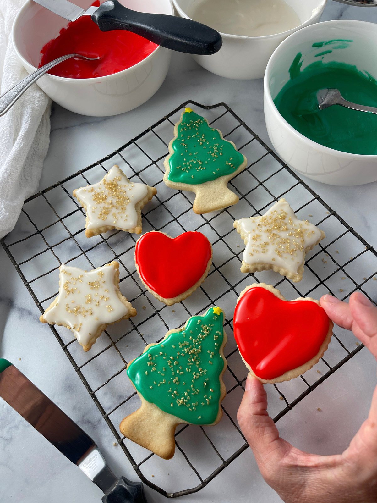 Freshly baked holiday cookies decorated with glossy red and green glaze on a wire rack.