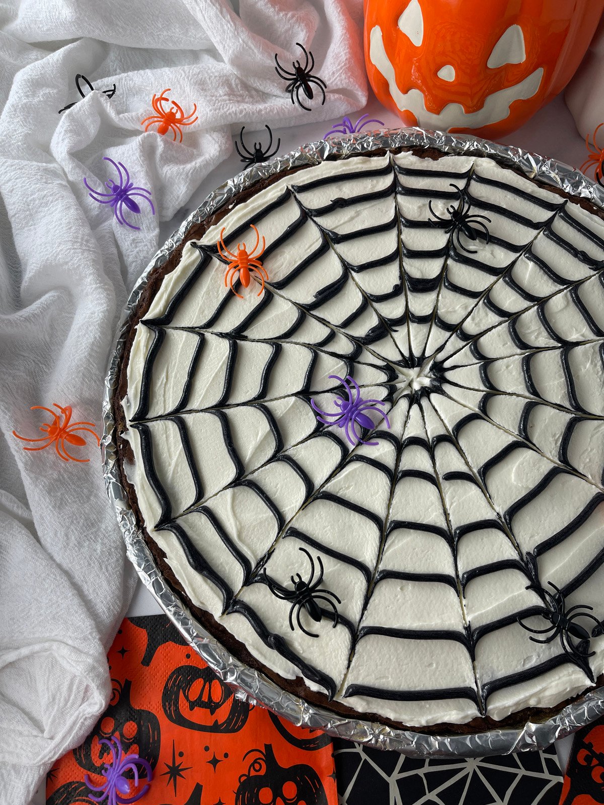 Halloween spider web cookie cake decorated with black frosting web, surrounded by festive decorations.