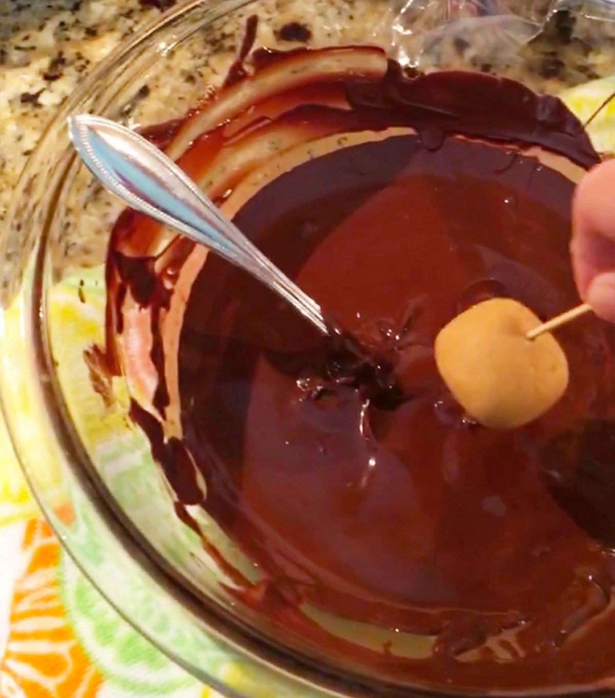 Process shot of dipping peanut butter balls into melted chocolate to make buckeyes.