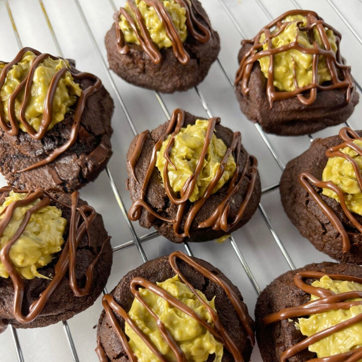 Cooling rack filled with freshly baked Dubai chocolate thumbprint cookies topped with pistachio cream filling and chocolate drizzle.