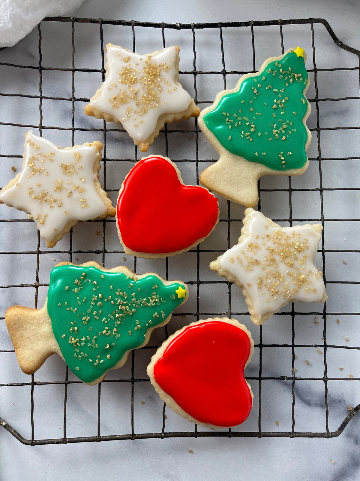 Cooling rack filled with freshly iced sugar cookies decorated with shiny red and green glaze.
