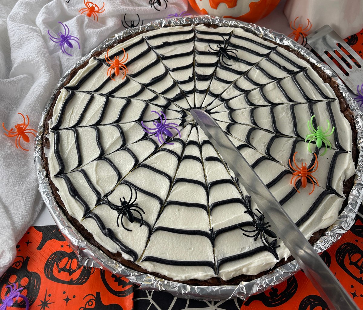 Cookie cake decorated with spider web frosting, displayed with plastic spiders.
