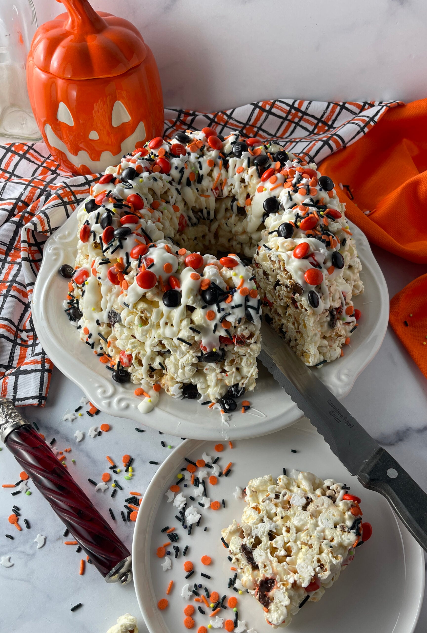 Halloween popcorn bundt cake cut into with one piece served on a white plate beside the cake.