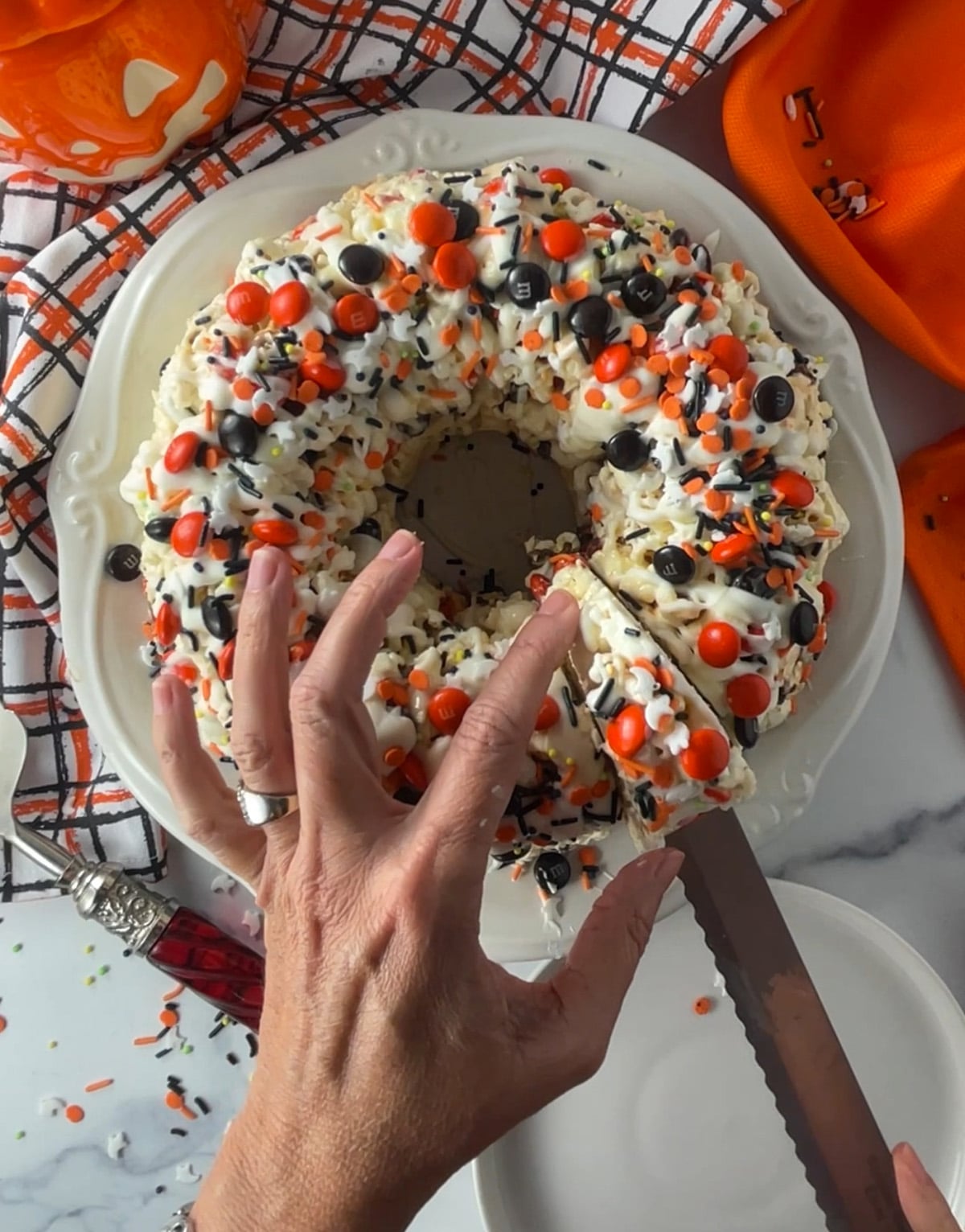 Slicing a piece of Halloween popcorn bundt cake topped with white chocolate drizzle, candy, and sprinkles.