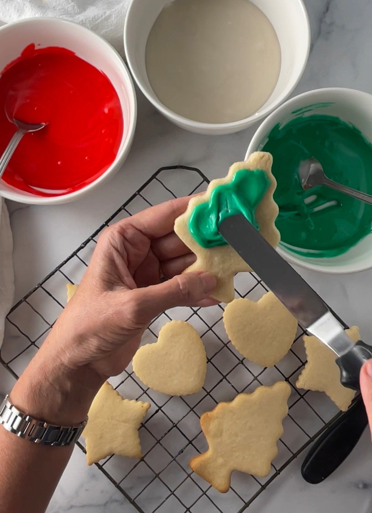 Freshly baked holiday cookies decorated with glossy red and green glaze on a wire rack.
