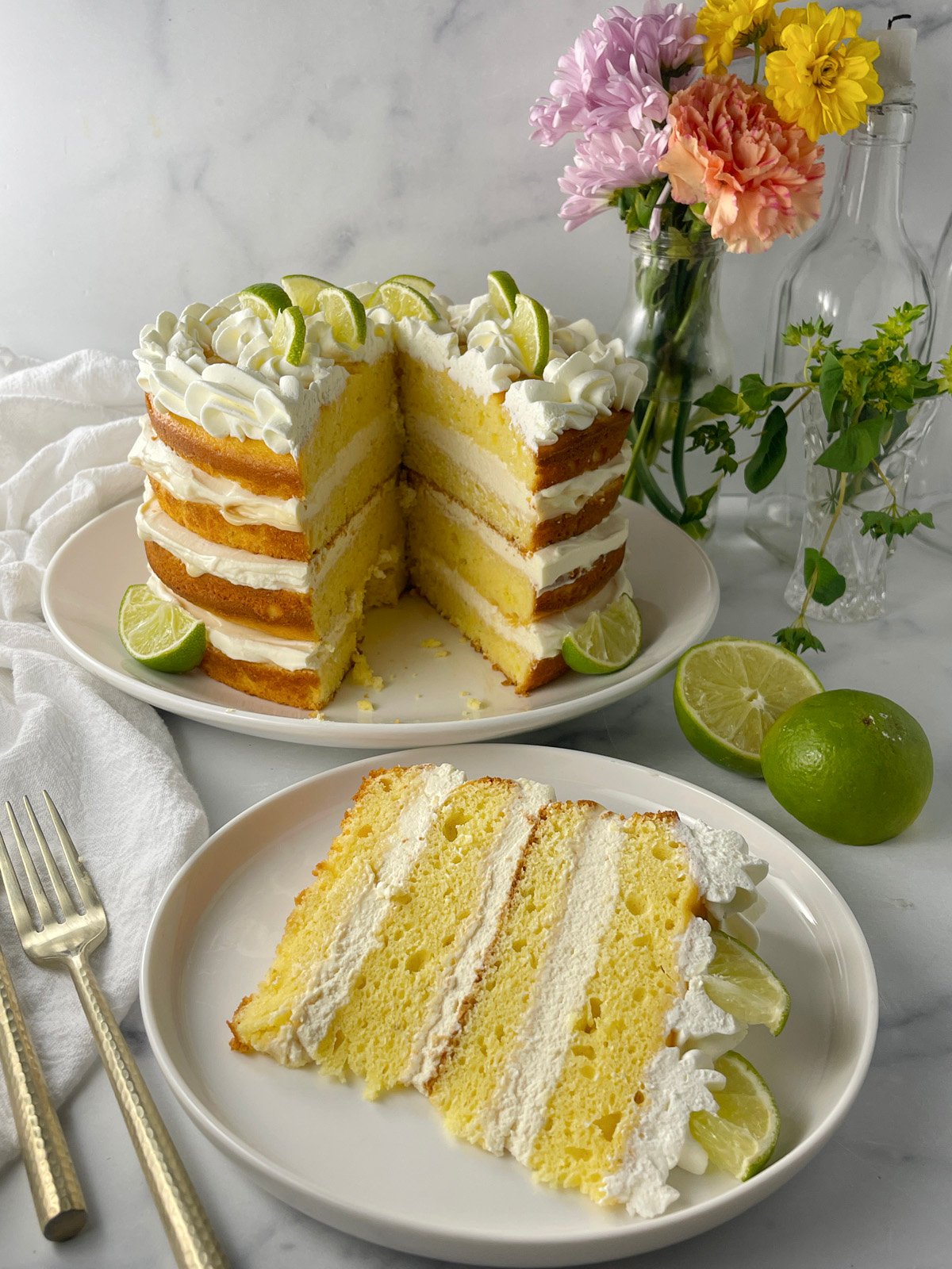 Overhead view of key lime layer cake decorated with piped whipped cream and lime triangles.