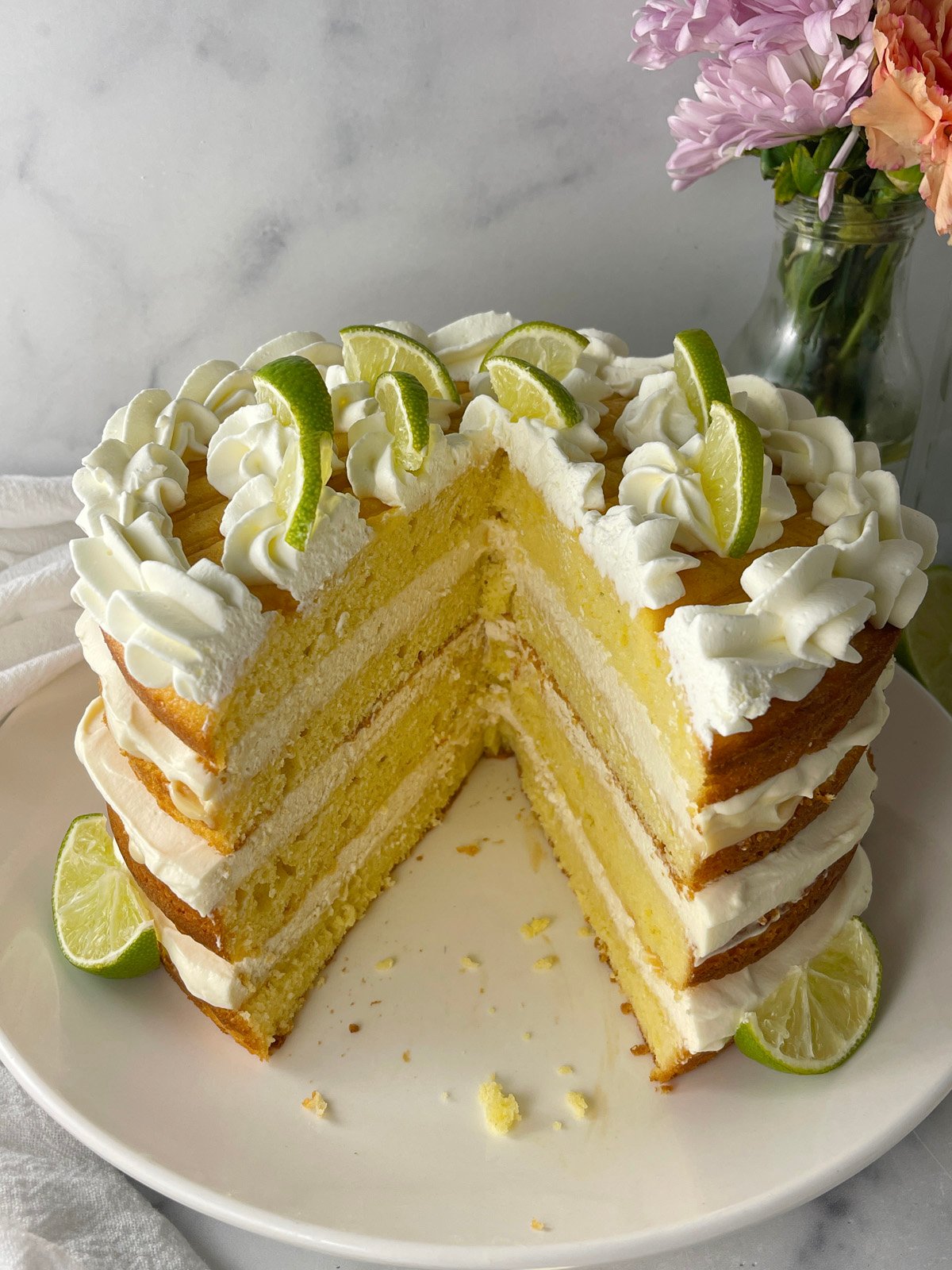 Whole key lime layer cake topped with whipped cream swirls and lime wedges on a cake stand.
