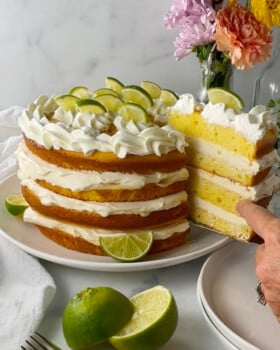 First slice of key lime layer cake being lifted out, showing moist cake layers with whipped cream filling and lime garnish.