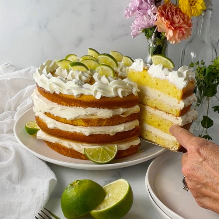 First slice of key lime layer cake being lifted out, showing moist cake layers with whipped cream filling and lime garnish.