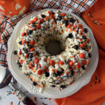 Halloween popcorn bundt cake on a white plate, drizzled with white chocolate and topped with colorful sprinkles and candy pieces.