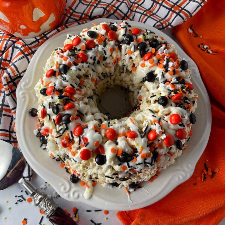 Halloween popcorn bundt cake on a white plate, drizzled with white chocolate and topped with colorful sprinkles and candy pieces.